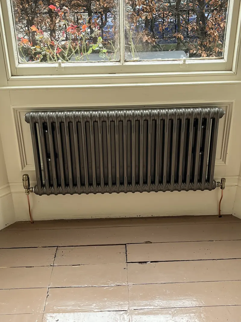 Column radiator fitted under a sash window
