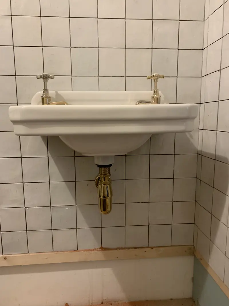 Traditional wall-hung basin fitted with brass taps and bottle trap